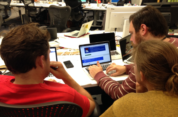 A group of user researchers gather around a laptop looking at the screen.