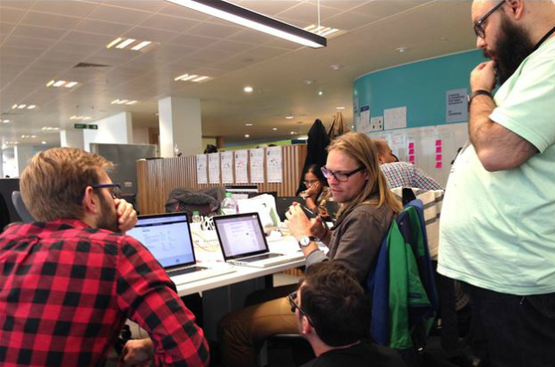 A group of people huddled around two laptops