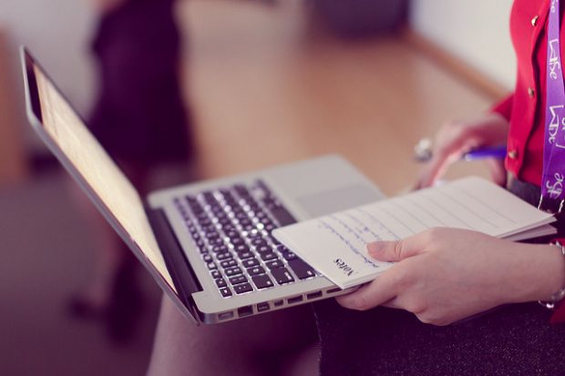 An image of someone working at a laptop with a notepad in their hand