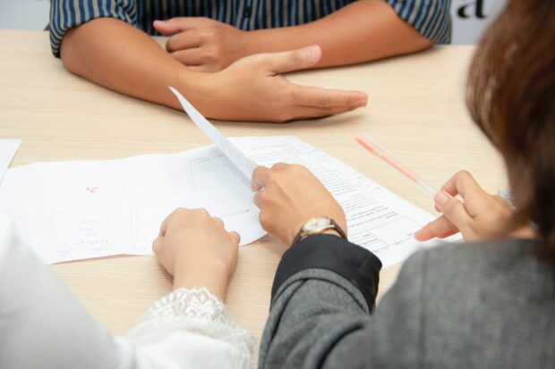 An image of the forearms of three people discussing a proposal