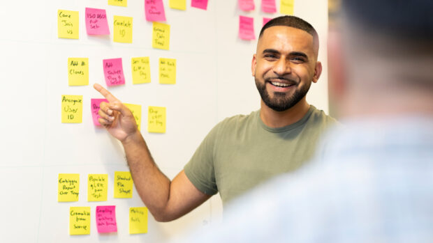 An image of a Home Office colleague in front of a whiteboard of post-it notes demonstrating a design process.