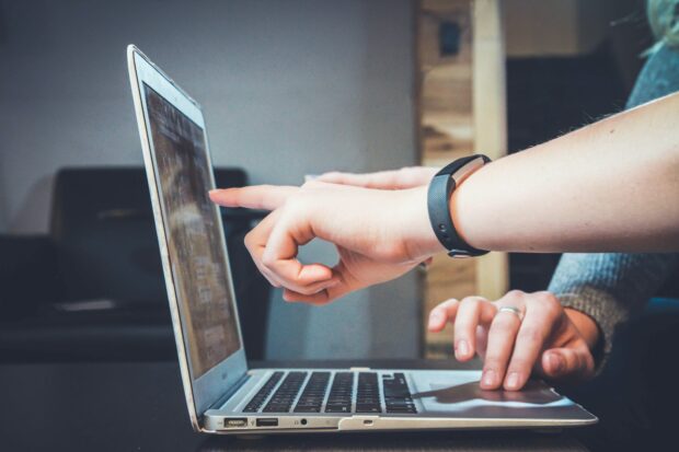 An image of the hands of two colleagues pointing to their work on a laptop.