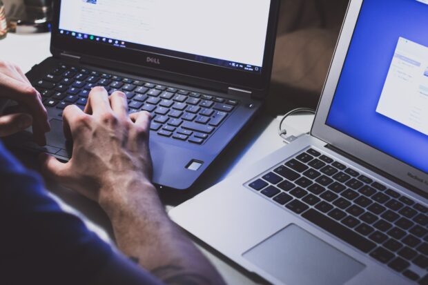 An image of a pair of hands working at two computers.